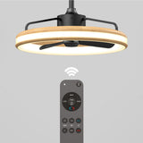 A modern ceiling fan with a circular LED light and wooden trim is shown above a remote control, indicating wireless operation. The background is light gray.