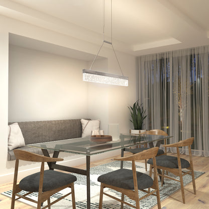 A modern dining room features a glass table, four wooden chairs with gray cushions, a gray cushioned bench, a patterned rug, sheer curtains over a large window, a potted plant in the corner, and an Artika Essence Bar LED pendant light overhead.