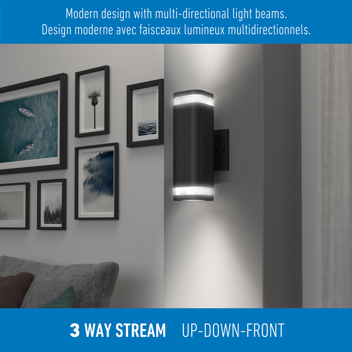 A modern black wall light fixture emits light upward, downward, and forward, illuminating part of a living room wall decorated with framed art above a gray couch. Text describes its multi-directional design.