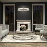 A modern living room features a white marble fireplace, two large windows, a round glass coffee table with flowers and books, white sofas, a plush rug, and the Artika Celebrity LED pendant light overhead.