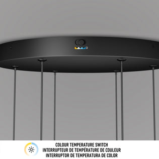 Close-up of the Artika Lewis modern LED pendant light 3 CCT in black, showing its colour temperature switch with three coloured buttons and a sun icon. Multilingual text below explains the switchs three settings.