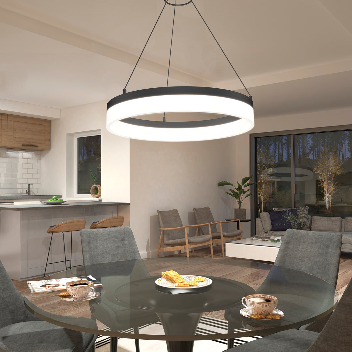 A modern dining area with a round glass table set for breakfast, gray chairs, a large circular pendant light overhead, and an open view to a cozy living room and kitchen with wooden accents.