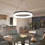 A modern dining area with a round glass table set for breakfast, gray chairs, a large circular pendant light overhead, and an open view to a cozy living room and kitchen with wooden accents.
