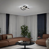 A modern living room at night with brown sofas, a round black coffee table, potted plants, large windows with curtains, and a contemporary ceiling light fixture with curving, illuminated bands.