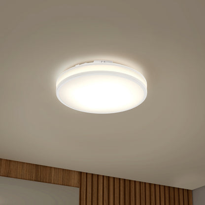 The Artika Hemisphere 15 in. LED flush mount light (5 CCT) casts a bright white glow on a beige ceiling above a wood-paneled wall.