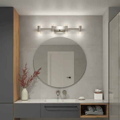 A modern bathroom features the Artika Mist modern LED bathroom vanity light (5 CCT) above a round mirror, white countertop, gray cabinets, and a vase with red branches. Rolled towels and tissues are displayed on shelves.