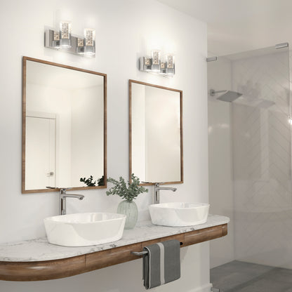 Modern bathroom with two vessel sinks on a marble countertop, each topped by a rectangular mirror and Artikas Ratio 2-light LED bathroom vanity light. A glass shower appears in the background, with greenery in a vase between the sinks.