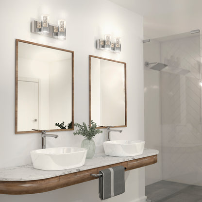 Modern bathroom with a double sink vanity, marble countertop, two framed mirrors, Artika Ratio 2-light LED vanity lights above each mirror, a white vase with greenery, and a glass-enclosed shower in the background.