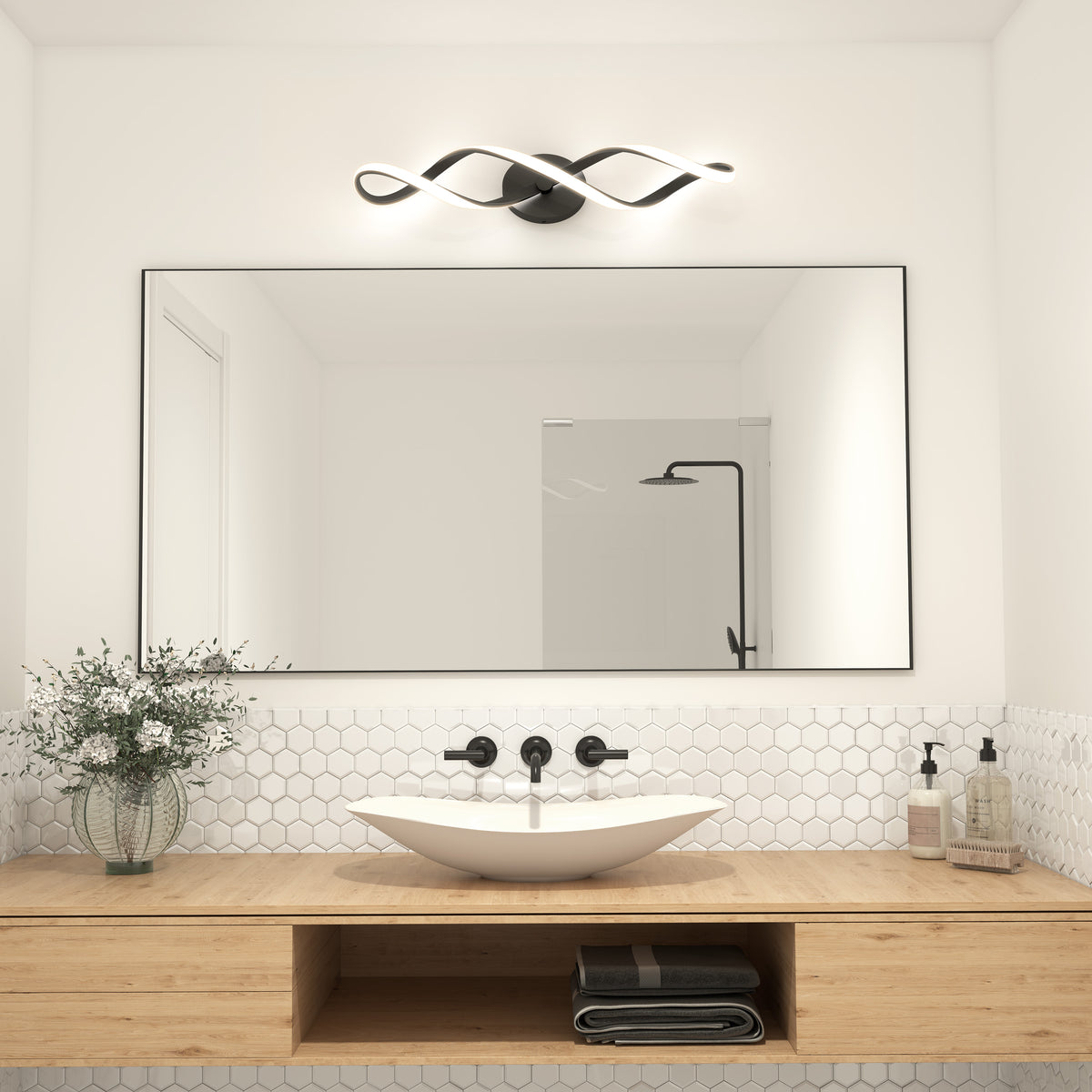 Minimalist bathroom with a large rectangular mirror, vessel sink, wall-mounted black faucet, wooden vanity, hexagonal white tile backsplash, modern wavy light fixture, and glass vase with greenery.