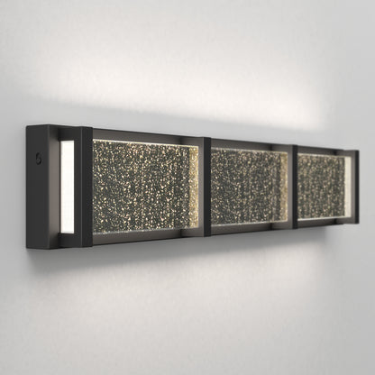 The Artika Subway Essence 3 LED bathroom vanity light features three illuminated sections with textured sparkling glass panels, a sleek black frame, and emits soft ambient light—perfect for a modern touch.