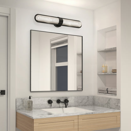 A modern bathroom features a marble countertop, rectangular sink, black faucet, and wall-mounted mirror. Above is the Artika Carat LED contemporary bathroom vanity light 3 CCT. Shelves hold folded towels and a soap dispenser.