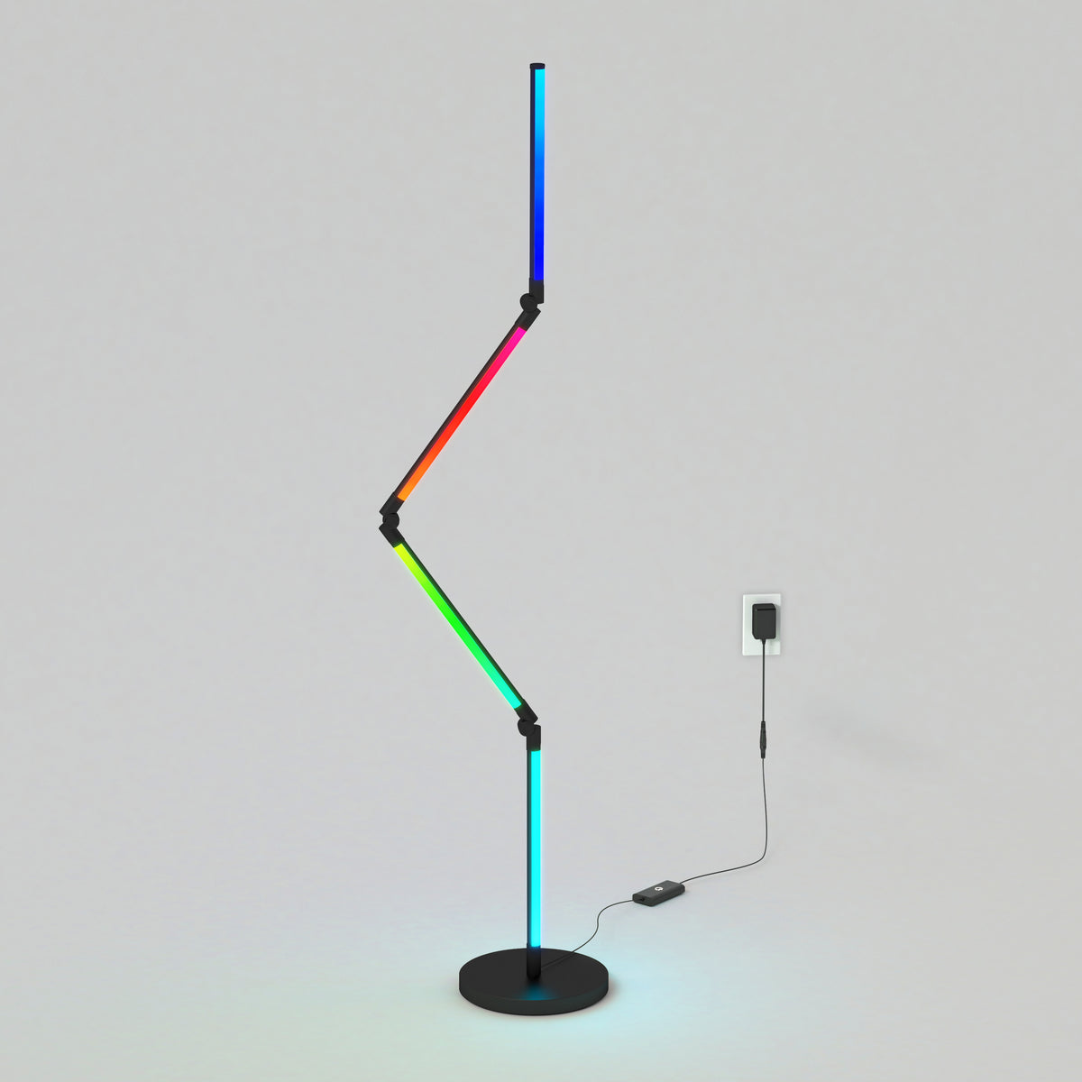 A modern, zigzag-shaped LED floor lamp with multicolor lights stands on a round black base, plugged into a wall outlet on a plain light gray background.