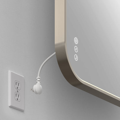 An unplugged white electrical plug sits near the Artika Royce Dimmable LED Mirror, 3 CCT, with illuminated touch controls, adjustable color temperature and defogger, mounted horizontally on a light-colored wall.