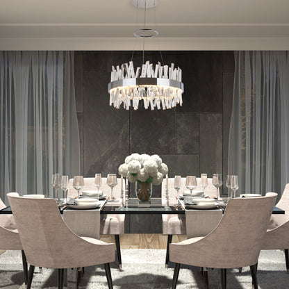 A modern dining room features a glass table for six, beige upholstered chairs, a white flower centerpiece, Artikas Enchanted LED pendant light, and floor-to-ceiling curtains against dark stone walls.