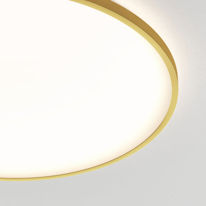 Close-up of a round, modern ceiling light with a gold rim, illuminating a white surface. Only part of the light fixture is visible in the top left corner against a neutral background.