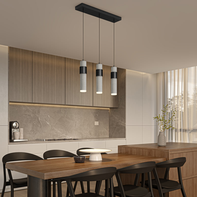 Modern kitchen with wood cabinetry, marble backsplash, and a built-in cooktop. A wooden dining table with black chairs sits beneath the Artika Barden 3-light LED pendant light. Natural light flows in through a large window with sheer curtains.