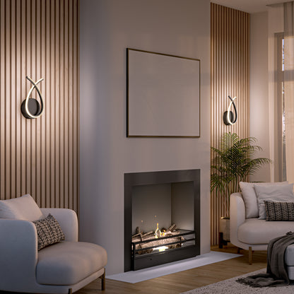 A modern living room featuring an Artika Gamma modern LED wall sconce 5 CCT, fireplace, two armchairs, wood paneling, abstract wall art, a potted plant, and neutral decor. Warm light adds a cozy and inviting ambiance.