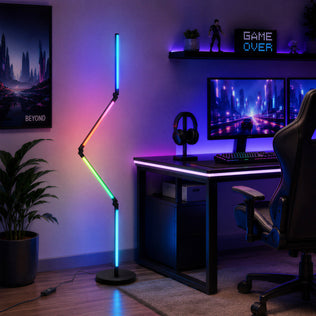 A modern gaming setup includes dual monitors, a gaming chair, and the Artika Fitch RGB LED floor lamp in a dimly lit room.