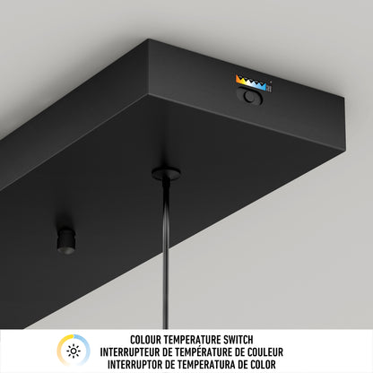 Close-up of the black Hanson 4-light LED pendant by Artika, featuring a color temperature switch and icon, suspended by two cables. Text below explains the 5 CCT switch in English, French, and Spanish.