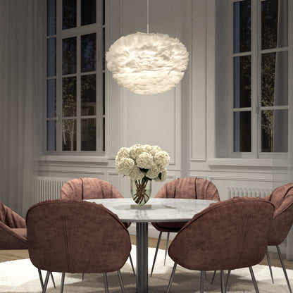 A modern dining room featuring a round marble table, six mauve upholstered chairs, a vase of white flowers, large windows, and the Artika Plume LED pendant light hanging above.