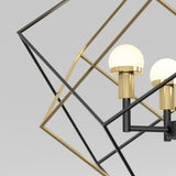 Close-up of a modern geometric chandelier featuring a black and gold metal frame with two round frosted glass bulbs against a plain light gray background.