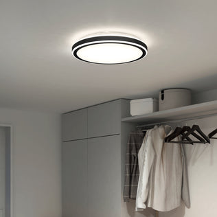 The Artika Altitude 15 in. LED modern flush mount light (5 CCT) is installed in a minimalist room with light gray walls, a wardrobe, and a clothes rail for coats and hangers. Storage boxes sit on a high shelf above the wardrobe.