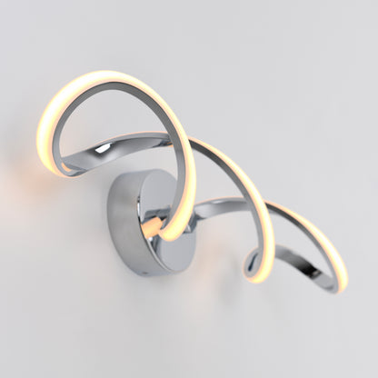 The Artika Swirl modern LED bathroom vanity light features two curved chrome arms with integrated LEDs, creating a soft, warm glow on a plain white wall.