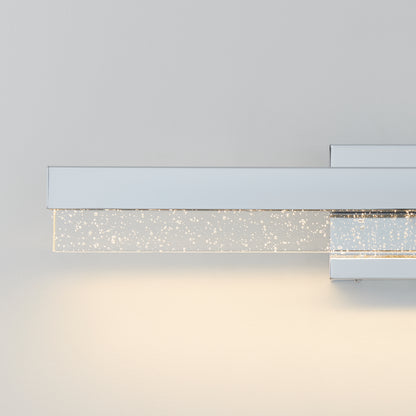 The Artika Essence Bubble Bar LED bathroom vanity light features a sleek silver design and a rectangular glass bar filled with tiny bubbles, casting a soft glow against a light gray wall.