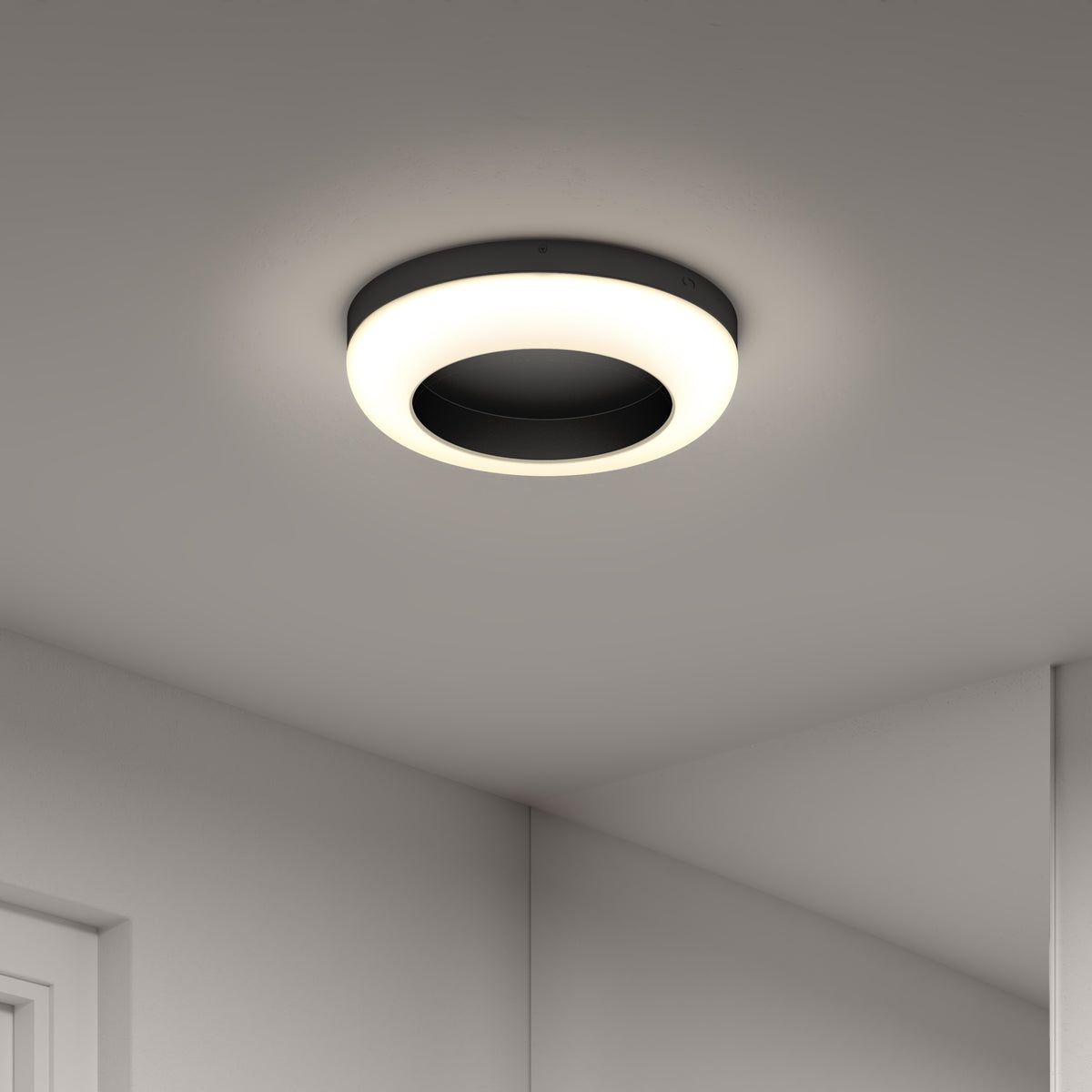 Modern circular ceiling light fixture with a glowing white ring and a dark central area, mounted on a smooth, light-colored ceiling with part of a wall and doorframe visible.