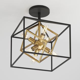 The Artika Imperium flush mount light features a modern geometric design with a black metal outer cube, an inner gold cube holding exposed bulbs, and a black base.