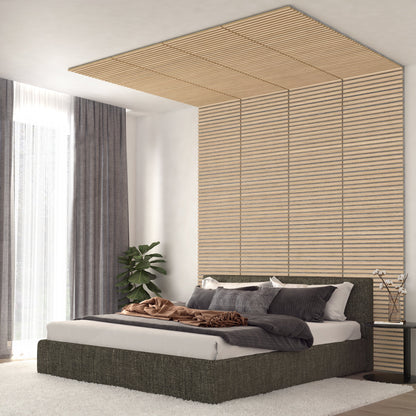A modern bedroom features a low platform bed, neutral bedding, and an Artika-CAN-dev Sonolok 15.5 ft sound-absorbing wall panel kit extending to the ceiling. Grey curtains frame tall windows, with a potted plant in the corner for greenery.