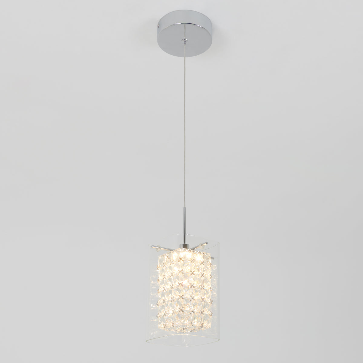 The Artika Crystal Cube 1-light LED pendant light features a chrome ceiling mount, slim cord, and cylindrical clear crystal shade that emits a soft glow, shown against a plain white background.