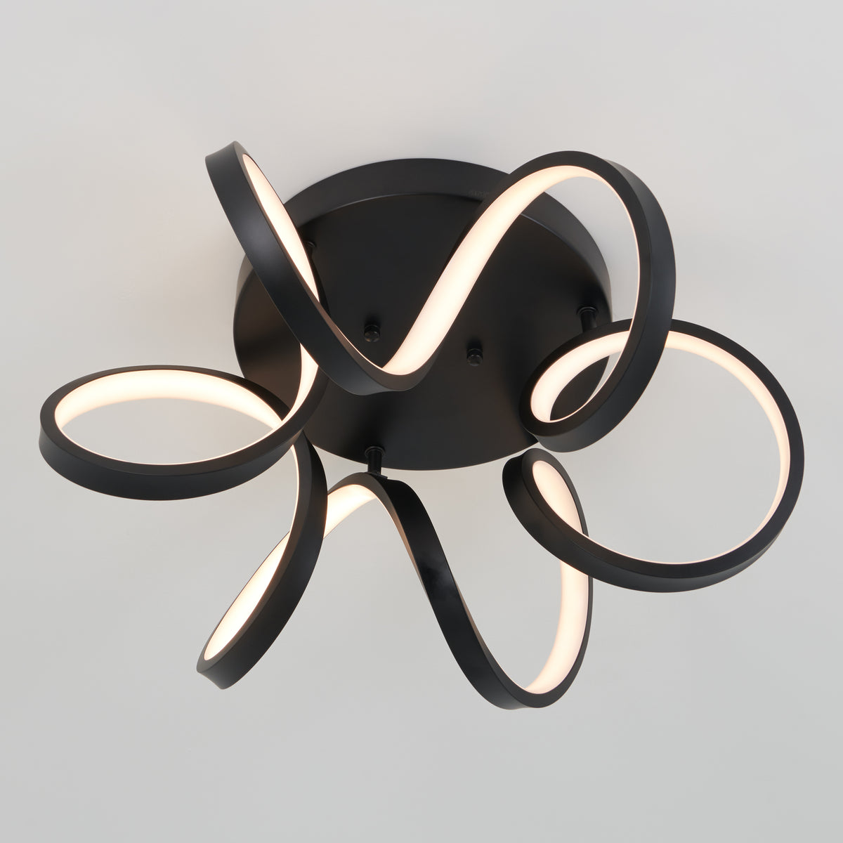 A modern ceiling light fixture with black, ribbon-like LED strips forming looping, abstract shapes, mounted on a round black base against a plain white ceiling.