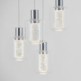 Four modern pendant lights with clear glass shades and metallic tops hang at different heights. The lights inside each shade emit a bright, sparkling glow, creating a contemporary and elegant look against a light background.