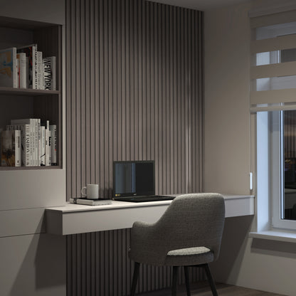 A modern, minimalist home office with a grey chair at a white desk, a closed laptop, a mug, books on shelves, and a window with layered blinds letting in soft evening light.