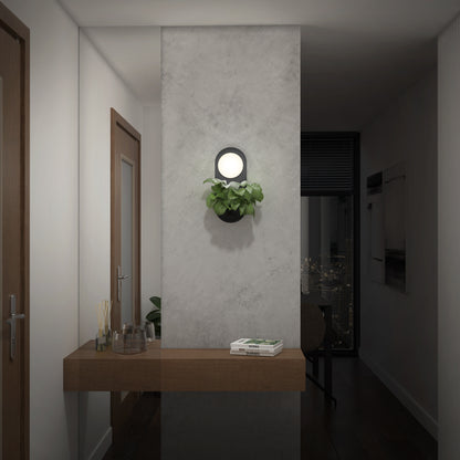 A modern hallway features the Artika Bloomfield LED modern mid-century wall sconce 5 CCT on a gray partition above a wooden console table with decor and a plant; a cityscape glows through the window in the adjacent dark room.
