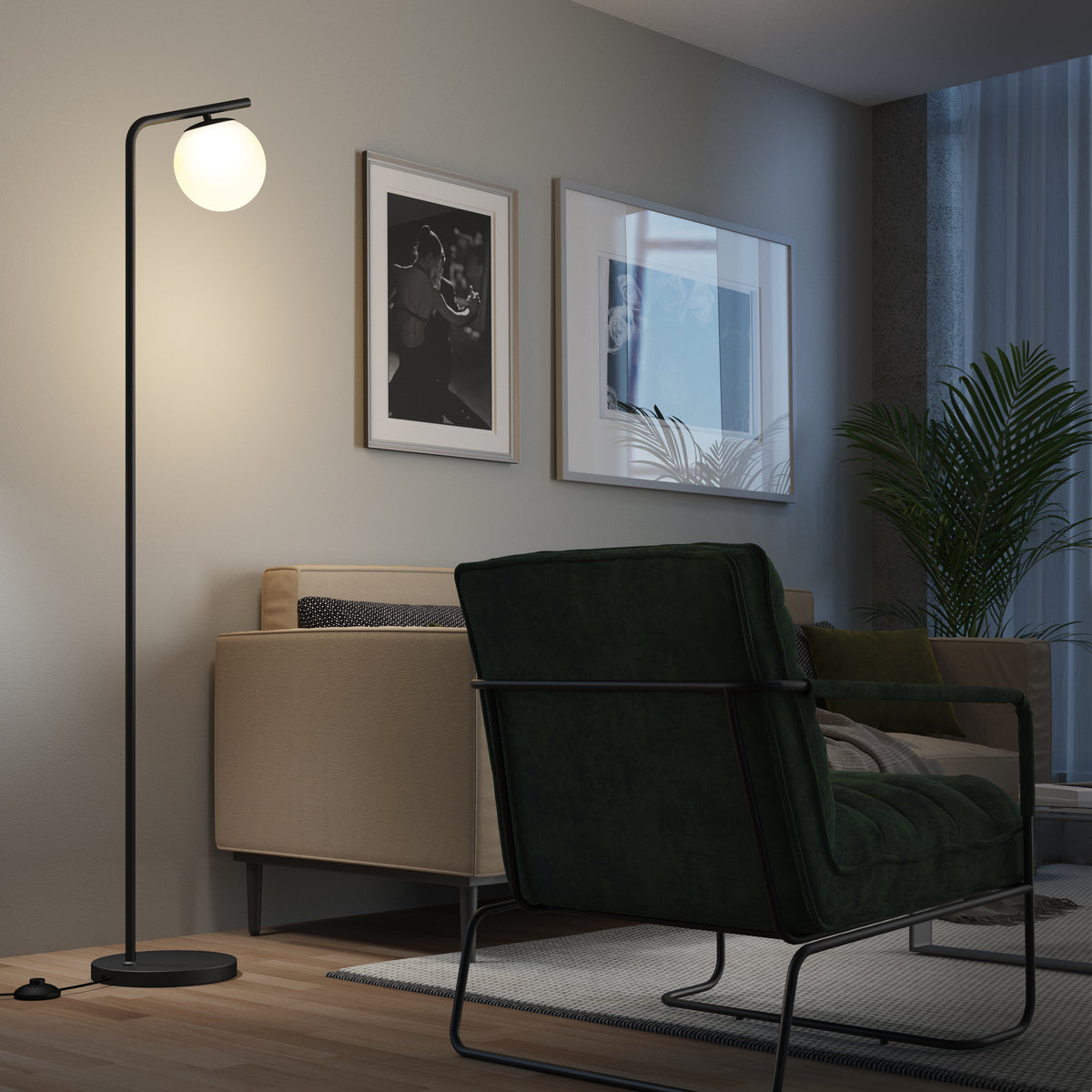 A modern living room with a green armchair, beige sofa, floor lamp with a round white shade, framed wall art, a potted plant, and a rug on wooden flooring. The lamp is turned on, creating a warm light.