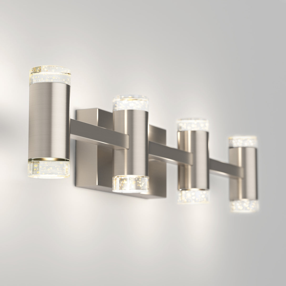 The Artika Mist modern LED bathroom vanity light 5 CCT features four cylindrical lights with clear textured glass ends on a brushed nickel rectangular base, offering stylish and versatile illumination for any bathroom.