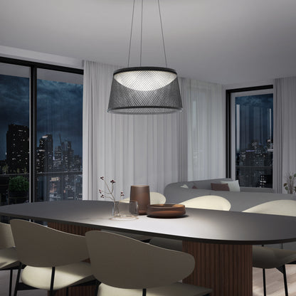 A modern dining room features a black oval table, light beige chairs, and minimalist décor. Large windows with sheer white curtains reveal a nighttime cityscape. Above the table hangs the Adrian LED pendant light 3 CCT by Artika.
