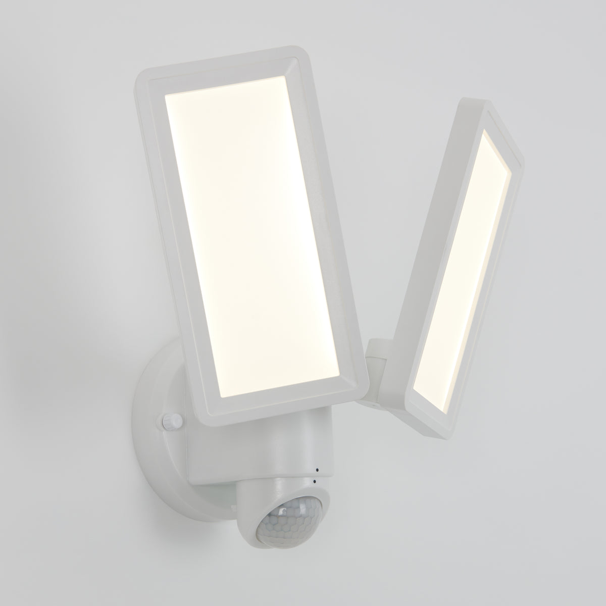 A modern white LED security light fixture with two rectangular adjustable panels, mounted on a wall, featuring a motion sensor at the base.