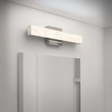 A modern rectangular wall light with a textured surface is mounted above a bathroom mirror on a white wall, casting a bright, even glow across the area.