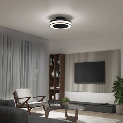 A modern living room with a gray armchair, coffee table, wall-mounted TV, wooden shelves, large window with sheer curtains, and the Artika Elton 19.4 in. LED modern ceiling fan (3 speeds, remote). A potted plant sits in the corner.