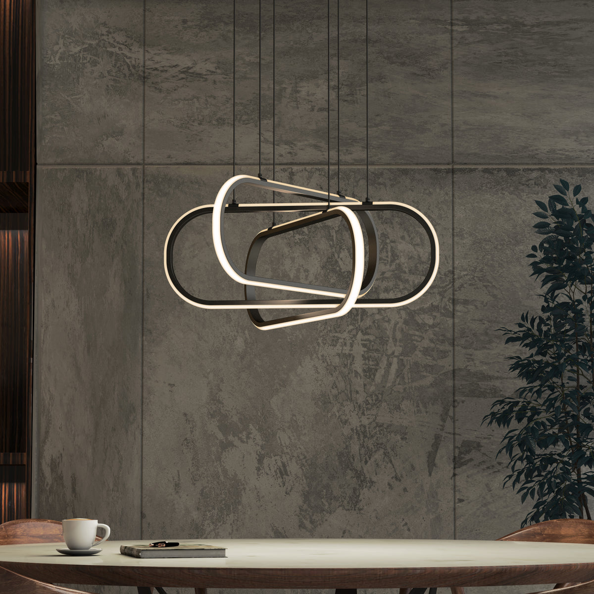 Modern dining room with a sculptural, geometric pendant light fixture above a round table; table holds a cup, saucer, and a book, with a plant and textured gray wall in the background.