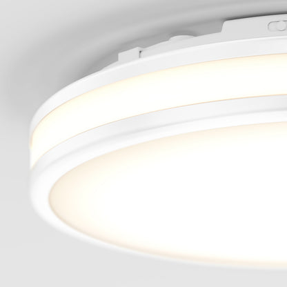 A close-up of the Artika Hemisphere 15 in. LED flush mount light (5 CCT) shows its modern circular white frame emitting a soft, warm glow on a plain white ceiling.