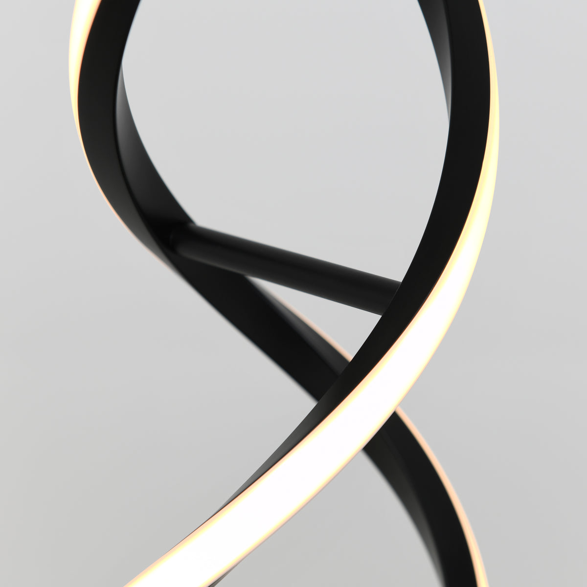 A close-up of a modern, abstract black lamp with a curving, twisted design and integrated LED light strip glowing softly against a plain white background.