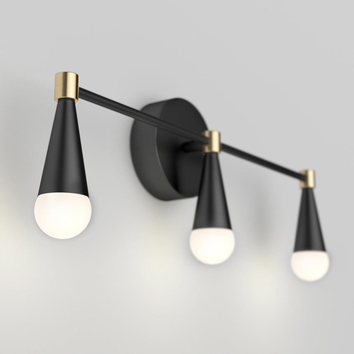A modern wall sconce with three cone-shaped black and gold light fixtures, each holding a round white bulb, mounted on a circular black base against a light gray wall.