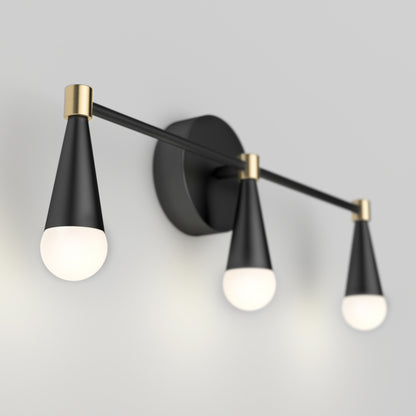 The Artika Wayden LED mid-century bathroom vanity light features three black cone-shaped holders with round white bulbs, gold accents, and a round black base, mounted stylishly on a light gray wall.