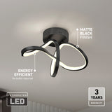 Modern ceiling light fixture with integrated LED, matte black finish, and a looping design. Text highlights energy efficiency (no bulbs required) and a 3-year warranty. Light is mounted on a white ceiling.