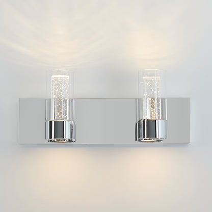 The Artika Ratio 2-light LED bathroom vanity light features two cylindrical glass shades on a sleek chrome base, casting soft up and down lighting on your wall for a modern look.