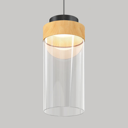The Artika Hanson 1-light LED pendant 5 CCT features a cylindrical clear glass shade, light wood accent top, and black mount, suspended from the ceiling against a plain gray background.